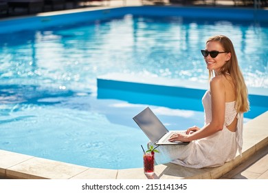 Self Employed Woman Doing Remote Work With Laptop Sitting Near Swimming Pool At Tropical Spa With Cocktail Drink. Freelancer Businesswoman Telecommuting With Team On Project From Luxury Resort.