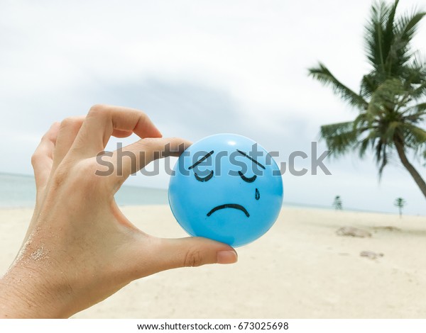 青いボールの上に 夏のビーチビューを持つ 自作の手で溺れる青い悲しい顔 の写真素材 今すぐ編集