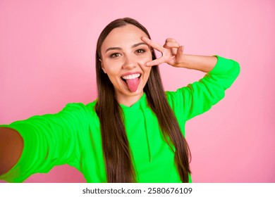 Self photo of charming attractive pretty sweet lovely girlfriend taking selfie fooling showing her tongue wearing yellow sweater while isolated over pink pastel background