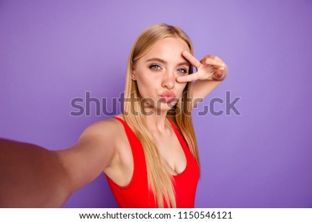 Self portrait of attractive cheerful blonde funny gorgeous playful flirting girl wearing red swim suit showing v-sign. Isolated over violet pastel background