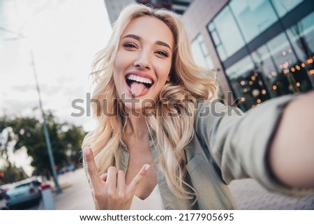 Self portrait of attractive cheerful childish wavy haired girl having fun showing horn sign fooling outside