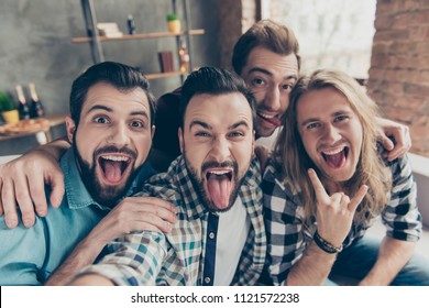 Self Portrait Of Four Attractive Comic Crazy Funny Foolish Guys With Hairstyle, Showing Tongue Out And Rock And Roll Symbol, Making Selfie On Smart Phone, Front Camera, Sitting On Couch In Livingroom