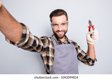 Self portrait of joyful cheerful man with stubble shooting selfie on front camera, showing pliers in arm, having fun, leisure, video-call, isolated on grey background
