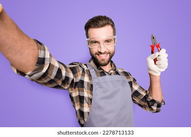 Self portrait of joyful cheerful man with stubble shooting selfie on front camera, showing pliers in arm, having fun, leisure, video-call, isolated on grey background