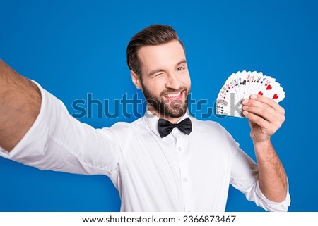 Self portrait of playful flirting croupier shooting selfie on front camera winking with eye demostrate present set of cards, isolated on grey background, having leisure video-call