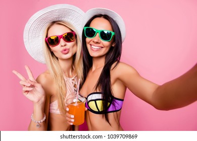 Self portrait of sexy, joyful, dreamy, charming, hot, stylish, pretty tourists shooting selfie on front camera, showing two fingers with pout lips, having alcohol beverage, isolated on pink background