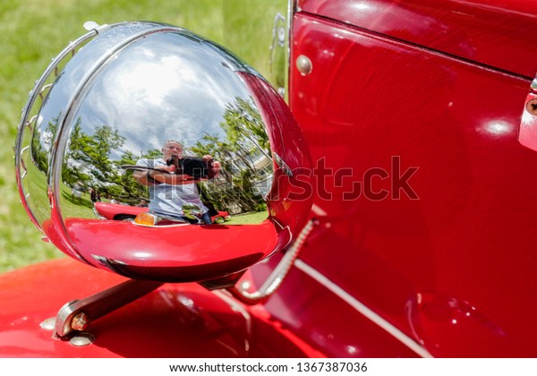 Self reflection of a\
camera man taking a close up detail photo on a shiny red classic\
car headlight lamp
