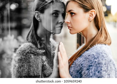 Self reflection portrait of amazing young girl in mirrored window. Unusual strange pretty woman person with sensual face looking at herself in showcase. Alter ego. Female state of mind. Other myself.