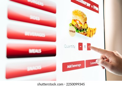 Self service order kiosk and digital menu in fast food burger restaurant. Touch screen in vending machine. Man using electronic selfservice technology and buying meal and paying.