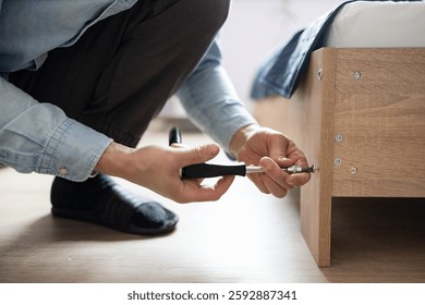 Self-assembly using a guide. House design. Close-up of a man's hands assembling a wooden bed using a hexagon to insert screws into the bed frame.Collection of wooden furniture. Husband for an hour.