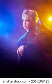 Self-assured Adult Blonde Middle Age Woman With Black Angel Wings. Model Posing In Studio On Black Background. Dangerous Cupid On Valentine's Day