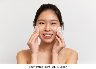 Selfcare Concept. Young Asian Lady With Beautiful Skin Cleansing Face With Cotton Pads, Making Daily Skincare Routine And Smiling At Camera While Posing Over White Background