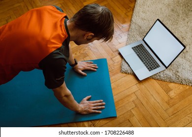 Self-care during stay at home COVID-19 Pandemic. Fitness training, stretching exercises online men at home with laptop. Attractive guy lying on fitness mat online yoga lessons blank laptop screen