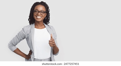 Self-confident African American corporate woman dressed in a grey blazer showing thumb up, isolated on a white background, with copy space for text.