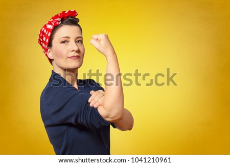 Self-confident middle aged woman with a clenched fist rolling up her sleeve, text space, tribute to american icon Rosie Riveter