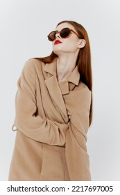 A self-confident stunning red-haired stylish girl in a coat and glasses poses in the studio on a white background. Advertising catalog shooting for the magazine - Shutterstock ID 2217697005