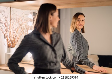 Self-confident Woman looking at her reflection into the mirror indoors. Beautiful interior design - Shutterstock ID 2118169394