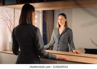 Self-confident Woman looking at her reflection into the mirror indoors. Beautiful interior design - Powered by Shutterstock