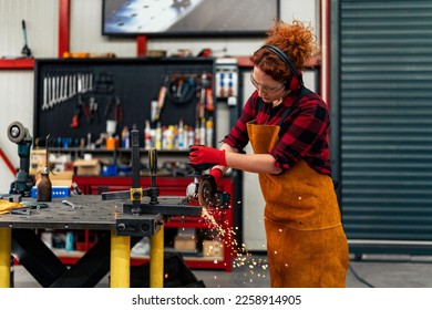 A self-employed worker is cutting a metal beam using a grinder, she is focused on her work and wearing protective gear her workshop in the background - Powered by Shutterstock