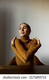 Self-esteem Concept. Vertical Image Of Arrogant Woman Hugging Herself Putting Arms Around Her Shoulders Sitting At Table Against White Wall. Cute Office Manager Warming Up During Break