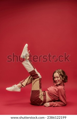 self-expression, full of joy girl in patchwork pants and cropped long sleeve sitting on red backdrop