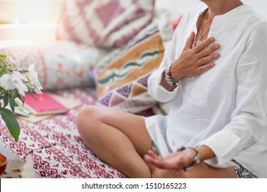 Selbstheilende Herz-Chakra-Meditation. Frau sitzend in einer Lotusposition mit der rechten Hand auf Herz Chakra und links Palme offen in einer aufnehmenden Geste. Selbstpflege zu Hause