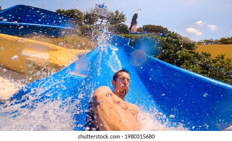 Selfie of a caucasian man sliding a water slide very fast, crashing and splashing into the pool. Having fun at a Water Amusement Park on summer vacation. Lifestyle, holidays activities.