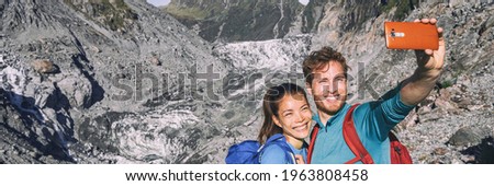 Selfie couple taking phone self-portrait on New Zealand by Franz Josef Glacier. New Zealand tourists smiling happy in nature in Westland Tai Poutini National Park. Horizontal banner landscape.
