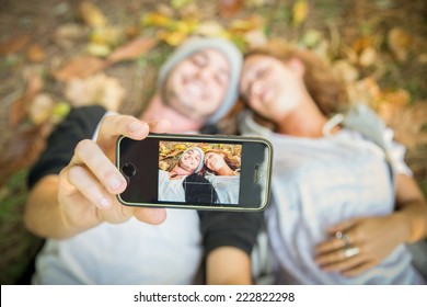 Selfie - Couple taking a self portrait while lying on meadow with yellow leaves