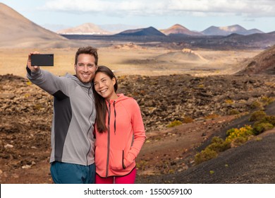 Selfie Couple Tourists Taking Self-photo Picture With Mobile Phone On Travel Vacation. People Summer Lifestyle Woman And Man Holidaying Visiting Lanzarote Timanfaya National Park, Canary Islands.