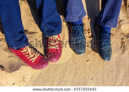 Selfie of feet, man and woman shoes on beach sand background, top view