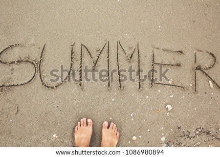 Selfie of foot with summer written in sand on beach