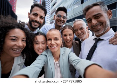 Selfie of happy business people taking photo with a phone. Multiracial teamwork taking a portrait of big group of colleagues. Corporative lifestyle of a diverse office workers in a financial center - Powered by Shutterstock