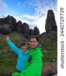 SELFIE: A happy couple of adventure tourists pose next to the Old Man of Storr. Smiling young woman and man are taking a photo of themselves at picturesque natural landmark on Isle of Skye in Scotland