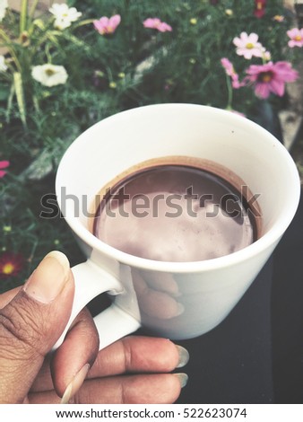 Selfie of hot chocolate on hand with cosmos flower in the garden