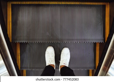 Selfie of  man feet in white sneaker shoes on escalator steps in the shopping mall, top view in vintage style