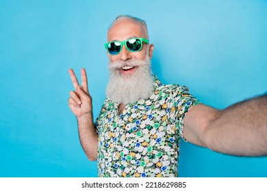 Selfie Photo Of Old Age Senior Grandfather Excited Hold Camera Wear Ray Ban Sun Glasses Showing V-sign Peace Good Mood Relax Isolated On Blue Color Background