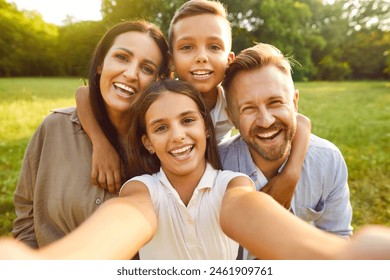 Selfie photo portrait of a happy family in nature. Beautiful joyful mother, father and children spending time together and relaxing in a fresh green summer park - Powered by Shutterstock