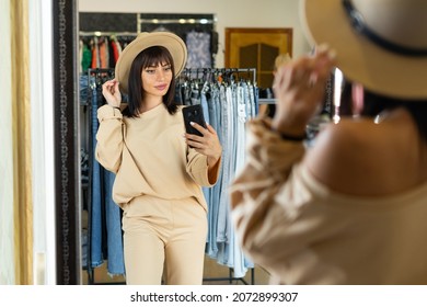 Selfie in a stylish hat in front of a mirror in a boutique or clothing store. Shopping in the mall on sale. Fitting room and a woman with a hat.