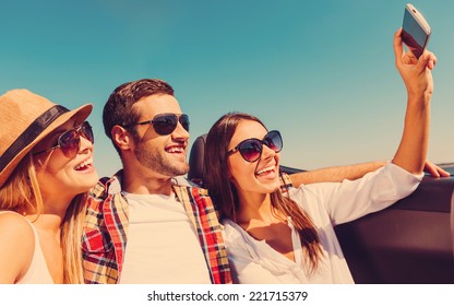 Selfie! Three Young Happy People Enjoying Road Trip In Convertible And Making Selfie