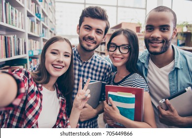 Selfie time! Four international students with beaming smiles are posing for selfie shot, caucasian attractive lady is taking, in school library building. Gathered, cheerful, smart and successful youth