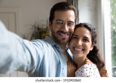 Selfie together. Happy millennial couple in love cuddling taking self picture at new home house flat. Excited young spouses hug holding phone looking at camera posing for portrait making video call - Powered by Shutterstock