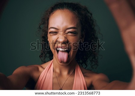Selfie, tongue out and young woman in studio with facial, expression or personality on green background. Face, emoji and crazy gen z model wink for silly profile picture, portrait or fun goofy post