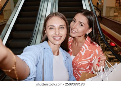 Selfie of two smiling girls with paper bags in hand, they standing next to escalator