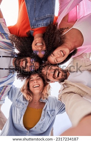 Selfie vertical of multiethnic group of friends looking at camera cheerfully embracing each other. Happy group of people in circle looking down. Low angle view. Copy space.