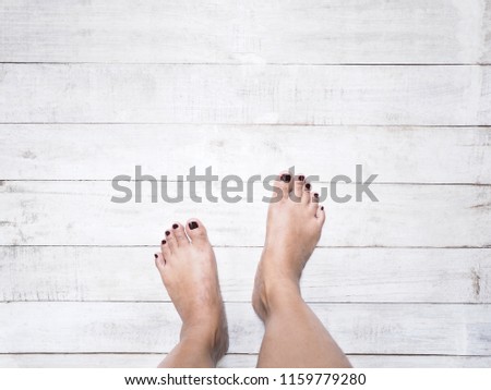 Selfie woman feet with dark red nails on white vintage wood white background.

