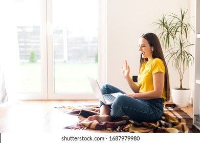 Self-isolation During Quarantine. Video Communication, Zoom. Young Positive Woman In A Yellow Casual T-shirt Communicates Via Video Communication Using A Laptop, She Waving Hello To The Screen