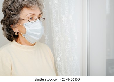 Self-isolation, Lockdown, Quarantine, Mental Health Of Elderly Concept. Side View Of Senior Sad Woman In Protective Medical Face Mask Standing Indoors And Looking Away. Copy Space.