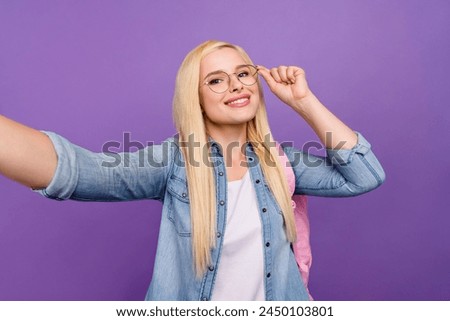 Self-portrait of attractive cheerful brainy girl touching specs going back to school isolated over bright violet purple color background