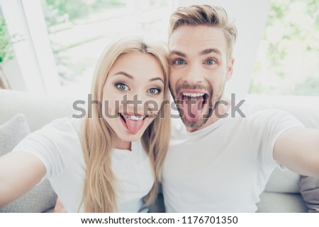 Self-portrait of beautiful lovely nice cute funky adorable excited dreamy stylish couple in house, showing tongues out, wearing casual white t-shirts